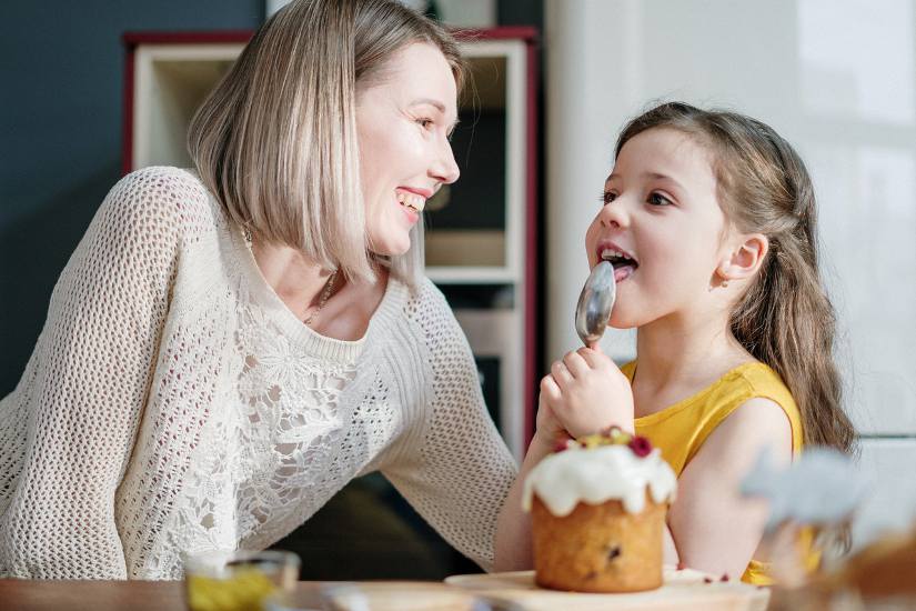Mom happily looks on as daughter enjoys cake