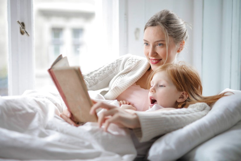 Mom reading out story to daughter lying beside her on the bed